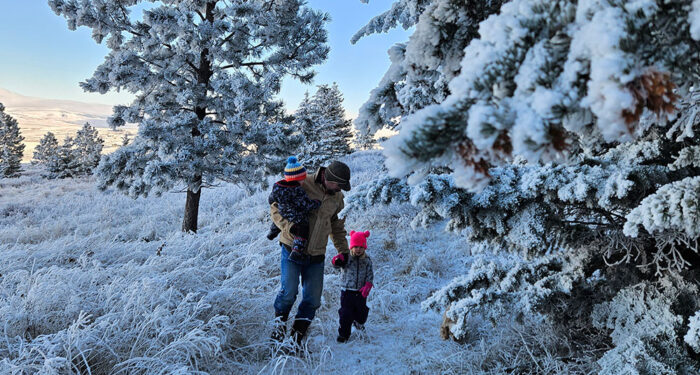 man carrying child and holding hand of a second child walking through the snow on a beautiful winter day