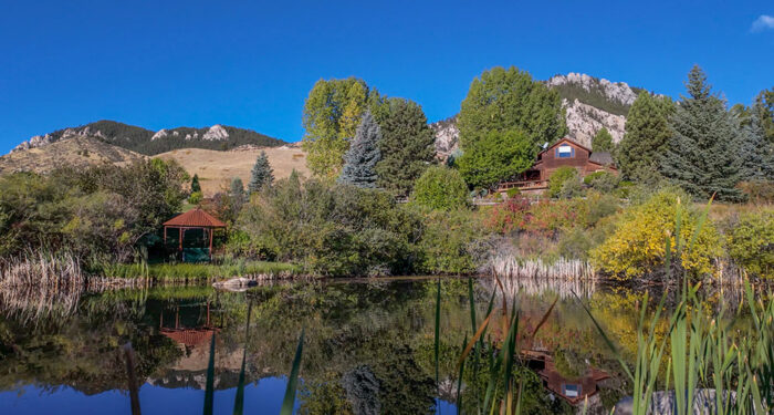 pond in foreground with ranch home and outbuildings and hills in the background