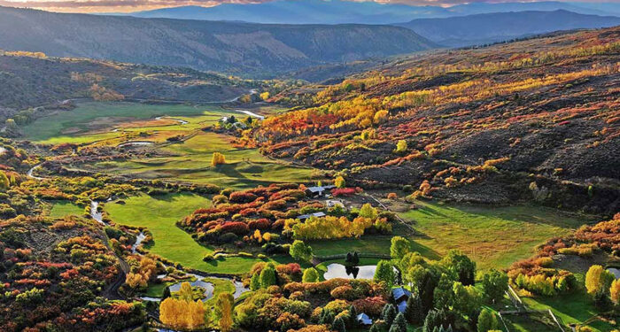 large vista of fall colors in homestead meadow with improvements and water