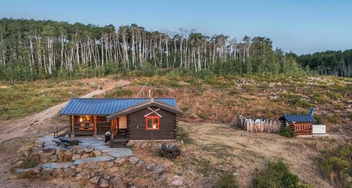 lit cabin in front of aspen grove on rocky hillside