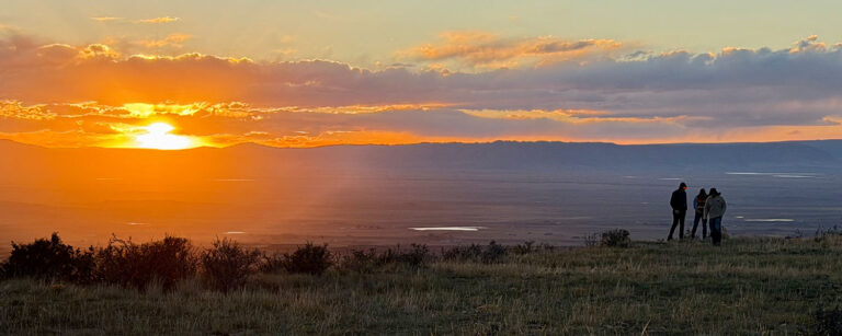 three adults look small against a vast landscape in the setting sun