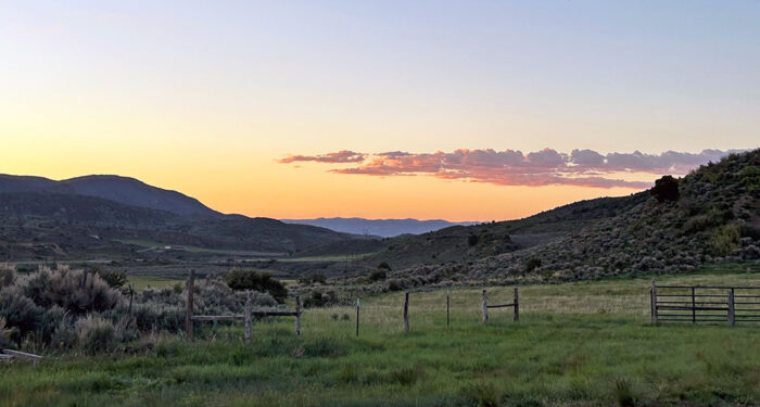 older barbed wire fence with open wire gate in foreground of distant hills and mountains at sunset