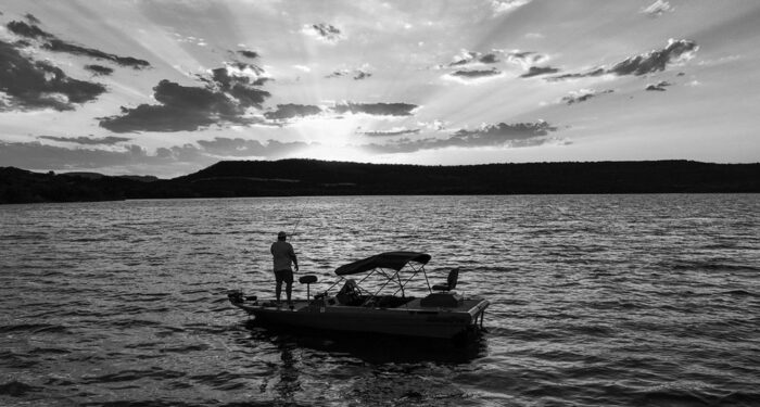 BW sunset of boat on lake with people standing and lounging