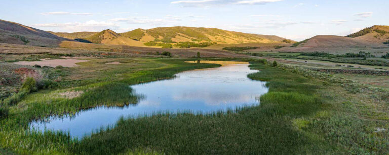 mountain valley meadow with pond and county road in the distant right
