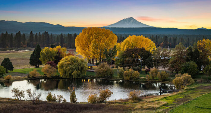 Fall colored trees behind pond with tall mountain peak in background at sunset