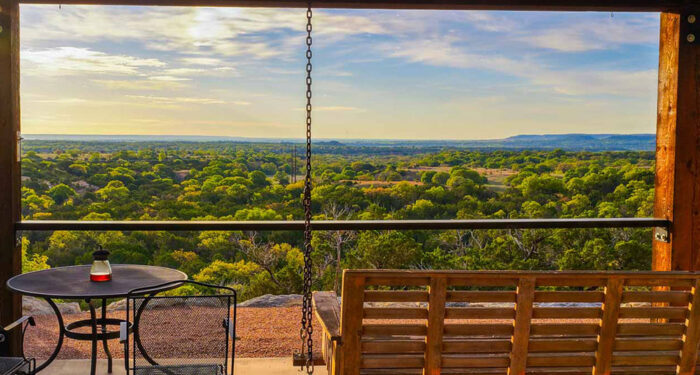 porch swing overlooking vista of brush-filled west texas landscape with blue cumulous cloud-filled sky