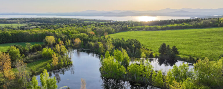 shrub lined pond wrapping around fields with distant lake and mountains