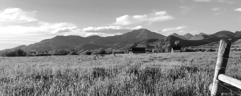 corner of fence on field with mountain backdrop in black and white