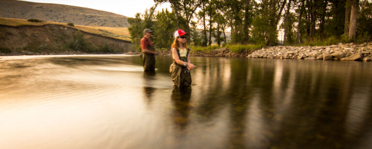dad and young daughter wearing waders and fly fishing in the river