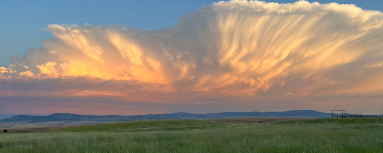striking clouds with color over a green pasture and distant mountains