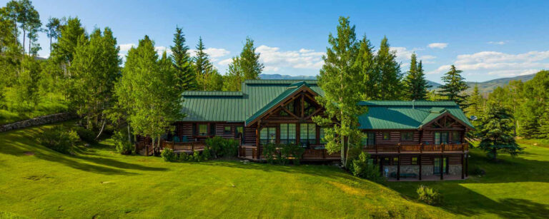 large wood home sits on hillside surrounded by coniferous trees and green grass