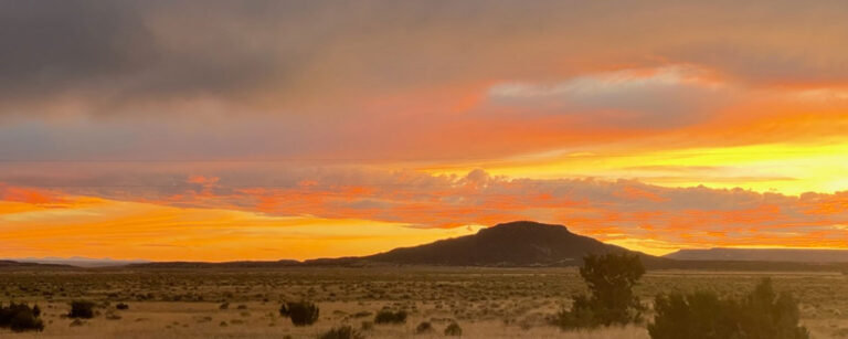 orange and yellow sunset over lone butte and bruch-covered land