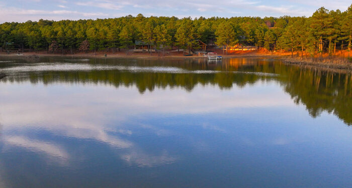 Large glassy lake with trees in the background with boat dock