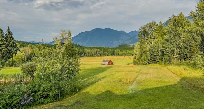 view of a homestead barn in a mountain valley with gold and green colors, dark blue mountains and cloudy sky