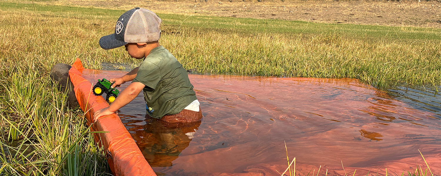 boy in orange tarp with water used as dams for flood irrigation