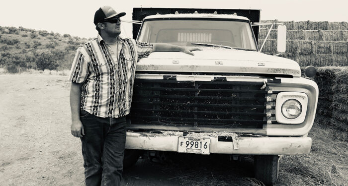 Oregon ranch and farm broker leans against old Ford truck in black and white photo