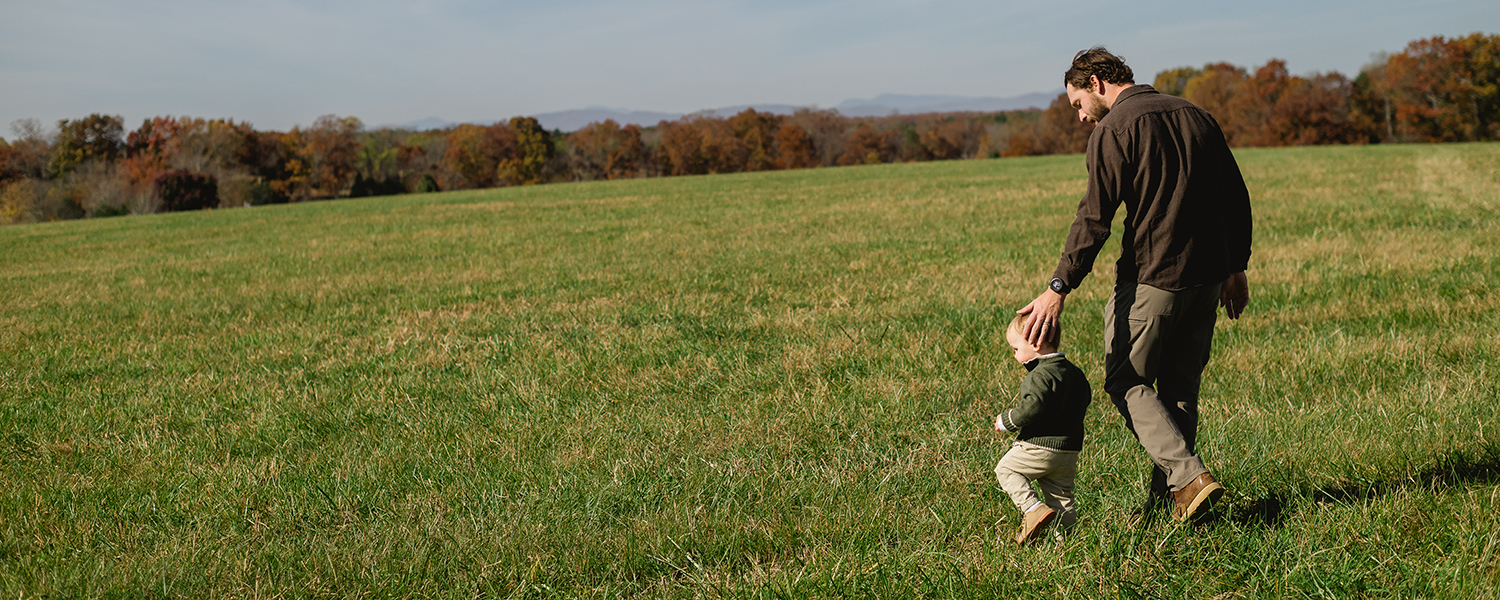 father and toddler walk across a pasture in Virginia