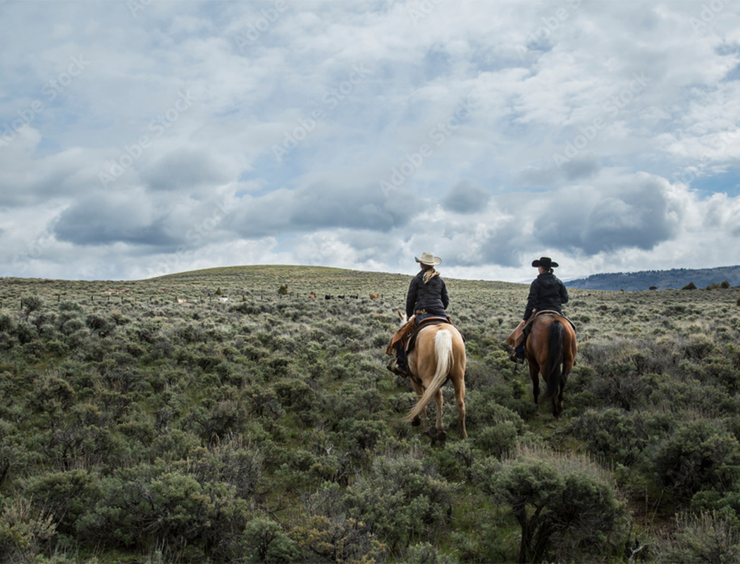 Two women on horseback riding through sagebrush