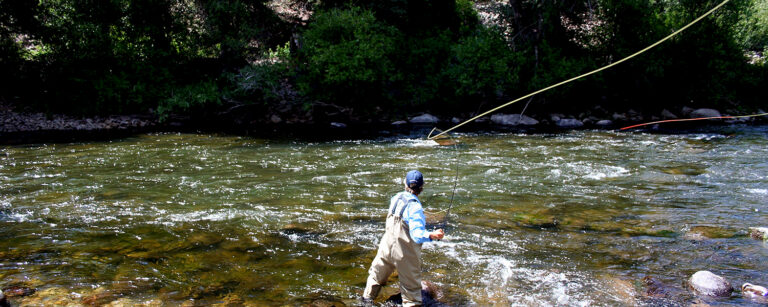 someone in blue shirt fly fishing on a recreational ranch with river